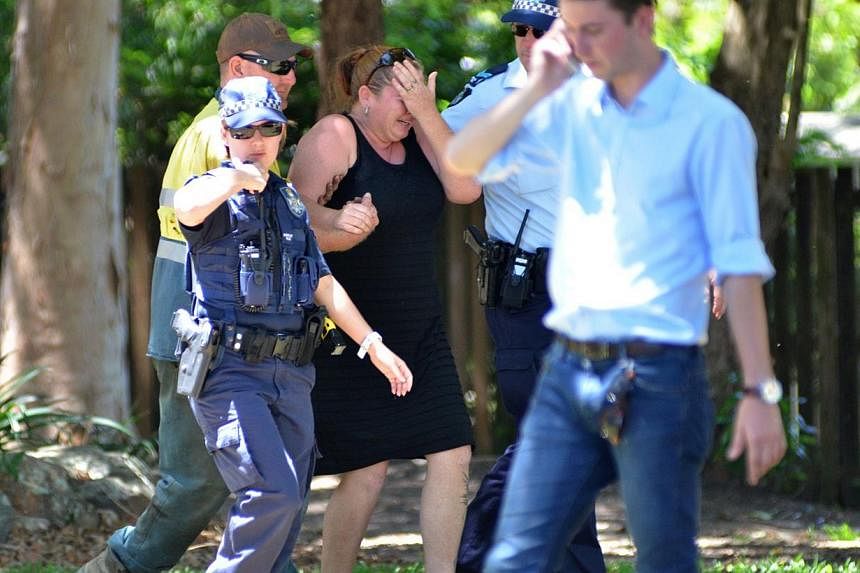 Police comforting a distressed woman at the scene where eight children aged between 18 months and 15 years were found dead at a home in the northern Australian city of Cairns, the police said on Dec 19, 2014, reportedly after a gruesome mass stabbing