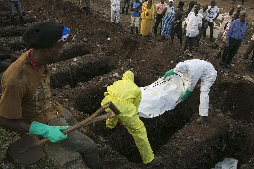 A grave digger watches as health workers carry the body of an Ebola victim for burial at a cemetery in Freetown on Dec 17, 2014. -- PHOTO: REUTERS