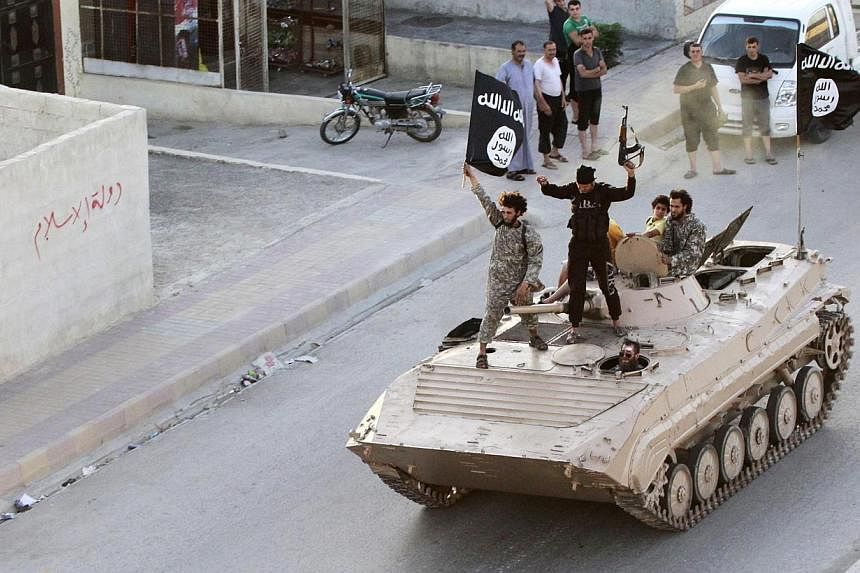 Men hold the flag of Islamic State in Iraq and Syria (ISIS) while taking part in a military parade along the streets of northern Raqqa province on June 30, 2014. -- PHOTO: REUTERS