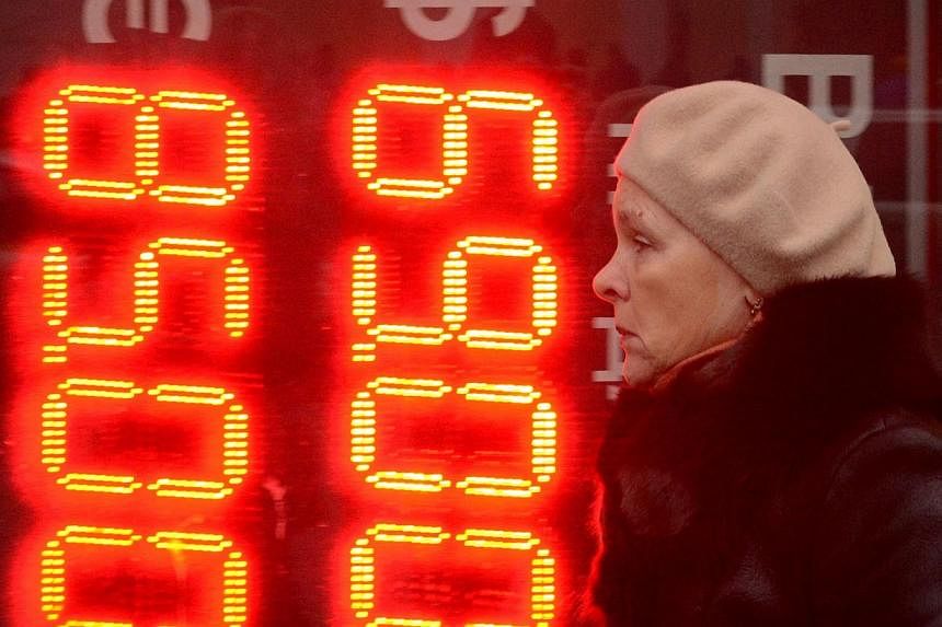 A woman walks past a board listing foreign currency rates against the Russian rouble outside an exchange office in central Moscow on Dec 16, 2014.&nbsp;&nbsp;Western companies are curtailing investments in Russia, repatriating funds and talking with 