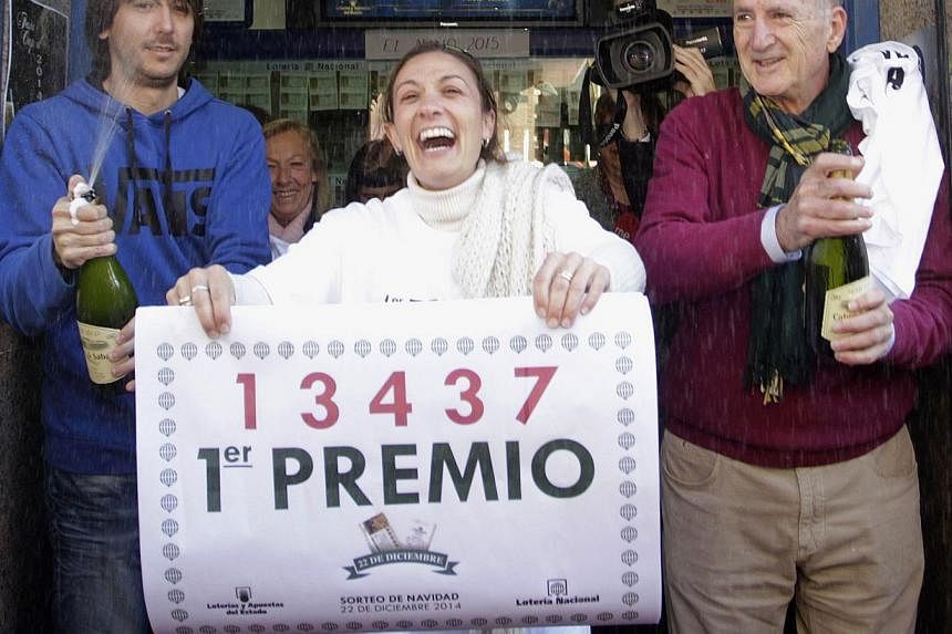 Lottery seller Raquel Carrasco (centre) holds a sign with the winning number of Spain's Christmas Lottery, El Gordo, in La Eliana near Valencia on Dec 22, 2014. -- PHOTO: REUTERS