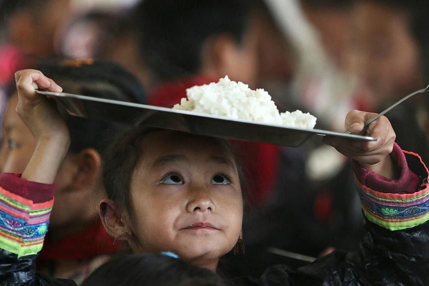 An ethnic Miao minority child wearing traditional costume carries a plate of rice during lunchtime at the village of Basha in Congjiang county, Guizhou province on Nov 27, 2014. -- PHOTO: REUTERS