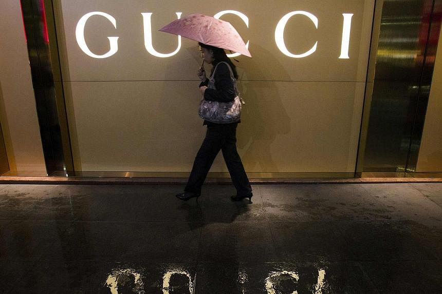 A woman holding an umbrella walks past a company logo of a Gucci boutique outside a shopping mall in central Guangzhou. The Italian fashion house said it would strengthen controls on its suppliers after a television programme showed Chinese employees