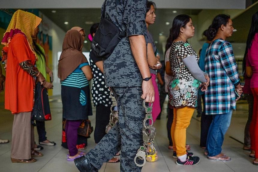 A Malaysian immigration officer (foreground) looks on as undocumented Indonesian workers queue for their papers to be processed before being deported back to Indonesia at Subang Airport in Subang, outside Kuala Lumpur on Dec 23, 2014. Malaysia deport