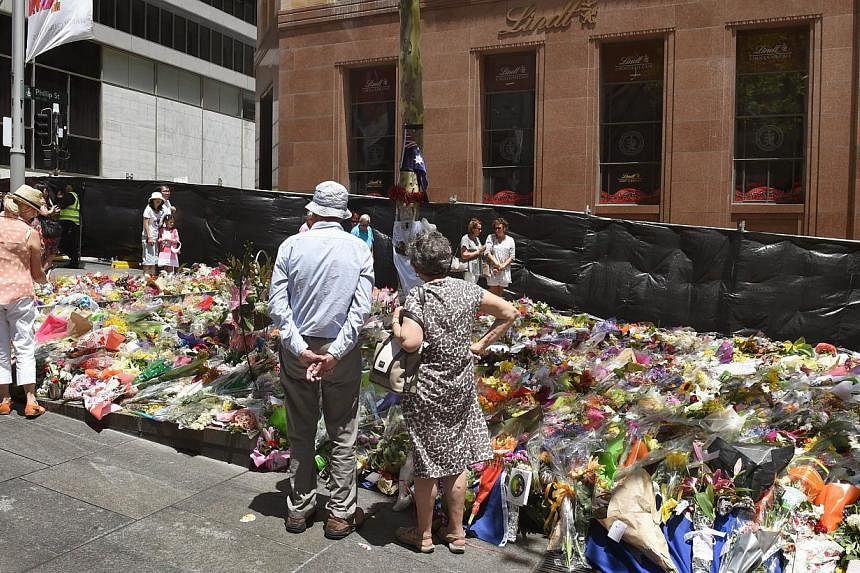 People look at the floral tributes left outside the Lindt cafe (rear) in Sydney's Martin Place, one week after a siege at the cafe which saw two hostages and the gunman killed on Dec 22, 2014. -- PHOTO: AFP