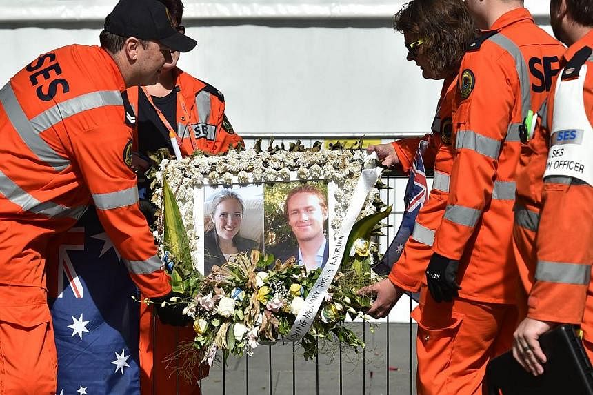 Volunteers removing a framed photograph of Katrina Dawson (left) and Tori Johnson (right) outside the Lindt cafe in Sydney on Dec 23, 2014, one week after a siege at the cafe which saw the two hostages and the gunman killed. -- PHOTO: AFP