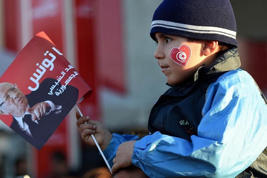 A child holds a flyer as supporters of Tunisian newly-elected President Beji Caid Essebsi celebrate after his victory on Dec 22, 2014 in Tunis.&nbsp;Tunisia's new leader Beji Caid Essebsi said the country has turned the page on dictatorship after a p