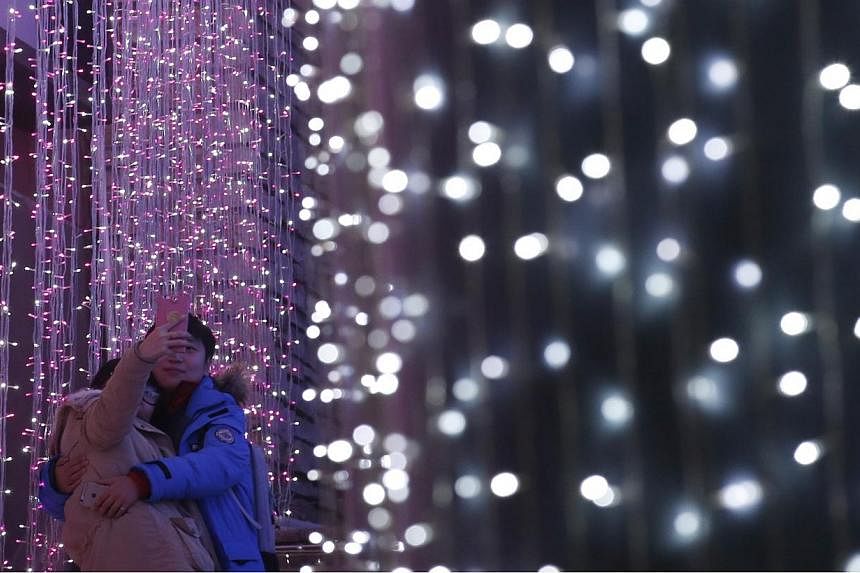 A couple takes a picture in front of a light installation for Christmas celebrations in Beijing on Dec 23, 2014. -- PHOTO: REUTERS&nbsp;