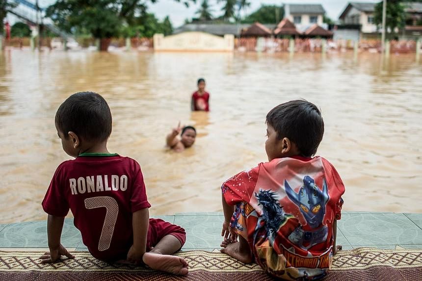 Two boys look on as their friends play in floodwaters in Pengkalan Chepa, near Kota Bharu on Dec 27, 2014.&nbsp;The number of people evacuated due to Malaysia's worst-ever floods jumped to more than 160,000 on Saturday, as Prime Minister Najib Razak 