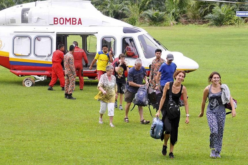 Tourists being escorted from a helicopter after they were evacuated from the National Park in Kuala Tahan to Jerantut, Pahang, on Dec 25, 2014. -- PHOTO: REUTERS