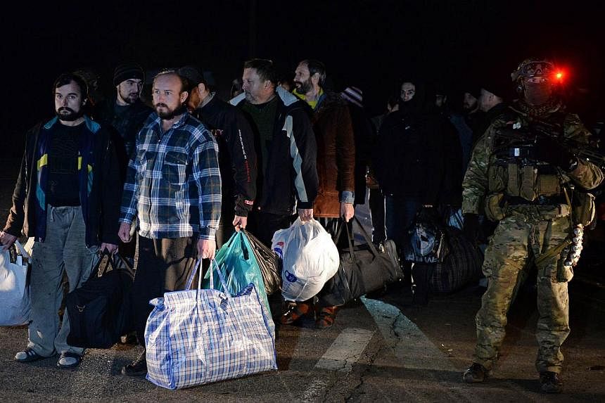 Prisoners from the self-proclaimed "People's Republic of Donetsk" stand next to a Ukrainain soldier during a prisoner exchange between Ukraine and pro-Russian rebels on December 26, 2014 in the eastern Ukrainian city of Yasinovataya, near Donetsk. --
