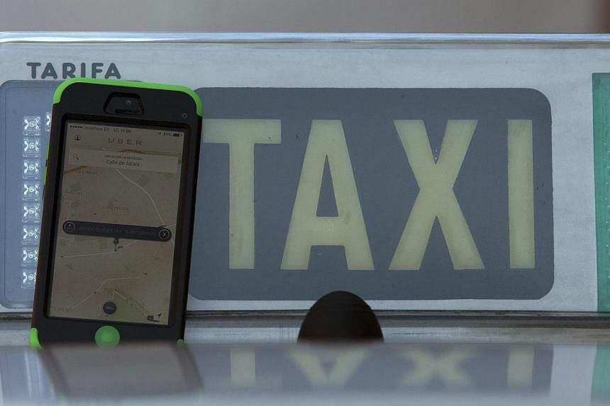 The car-sharing service app Uber on a smartphone next to a taxi sign is seen in this photo illustration taken in Madrid on Dec 10, 2014.&nbsp;Uber vowed Friday to keep operating in Spain despite a ban following a lawsuit by taxi drivers and said it w