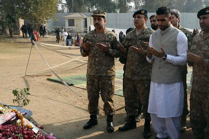 British boxer Amir Khan (second from right) prays along with Pakistani militarty officials at the memorial of the army-run school where 150 people were massacred by the Taliban, in Peshawar on Dec 29, 2014. -- PHOTO: AFP