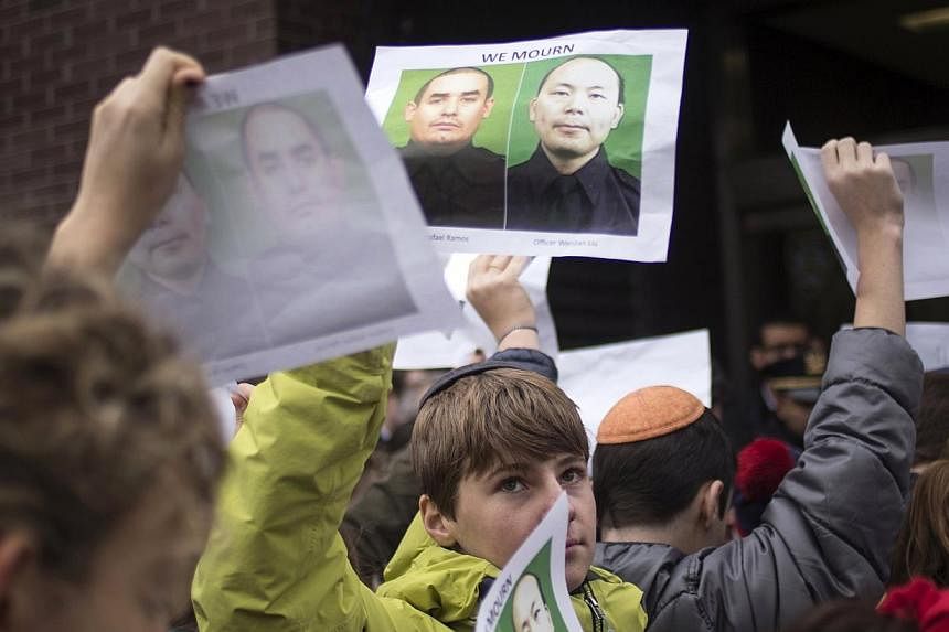 A school boy at an event to show support for police officers in New York on Dec 22, 2014, holds images of slain New York Police Department officers Wenjian Liu (right) and Rafael Ramos, who were shot and killed as they sat in a marked squad car on De