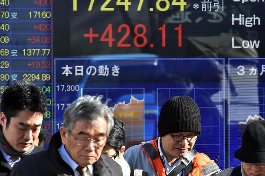 Pedestrians pass before a share prices board in Tokyo on Dec 18, 2014. -- PHOTO: AFP