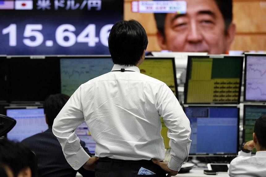 A man looks at monitors displaying Japan's Prime Minister Shinzo Abe and the yen's exchange rate against the US dollar in Tokyo on Nov 12, 2014. Japan's ruling coalition has approved a tax reform plan that will cut the corporate tax rate from April a