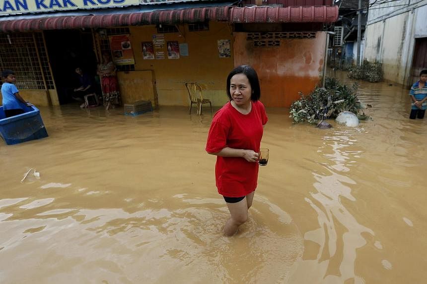 A woman holds her coffee cup as she walks through a flooded street on the outskirt of Kota Bharu in Kelantan on Monday, Dec 29, 2014.&nbsp;Malaysia's worst flooding in a decade has forced nearly a quarter of a million people from their homes, officia