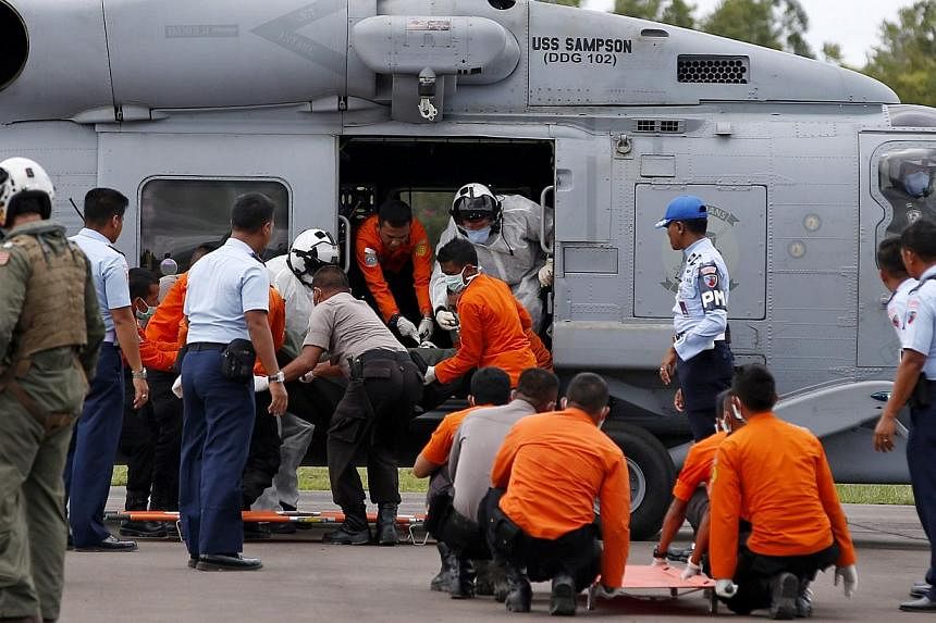 Crew members of a US Navy helicopter from the USS Sampson unload the remains of passengers from AirAsia QZ8501, recovered from the sea, at the airport in Pangkalan Bun, Central Kalimantan, on Jan 2, 2015. -- PHOTO: REUTERS