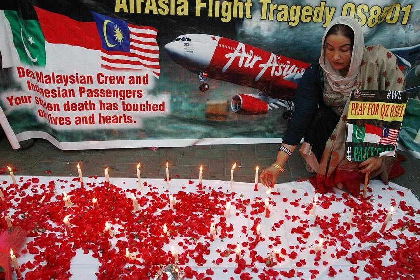 A member of the Lawyers Strategic Council of Pakistan holding up a sign as she lights candles during a vigil for the passengers of AirAsia Flight QZ8501 in Lahore on Jan 2, 2015. -- PHOTO: REUTERS