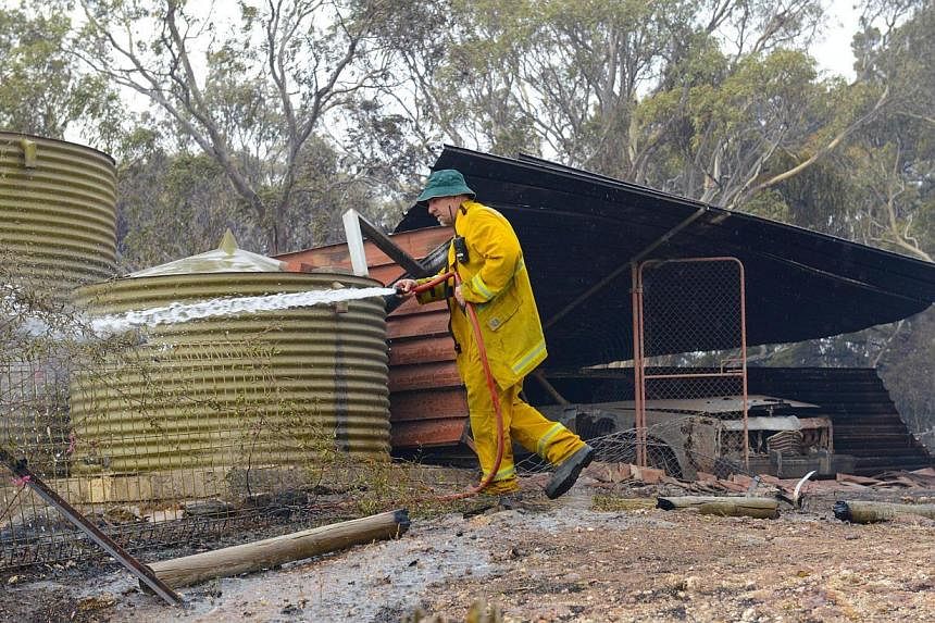 A Country Fire Service volunteer putting out spot fires next to a burnt out shed near One Tree Hill in the Adelaide Hills, north-east of Adelaide on Jan 3, 2015. -- PHOTO: AFP