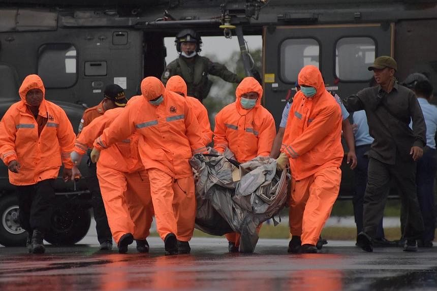 Members of an Indonesian search and rescue team carry items for investigation, found during the search operation for the missing AirAsia flight 8501, after being delivered by a Singapore Super Puma helicopter from the Republic of Singapore Air Force 
