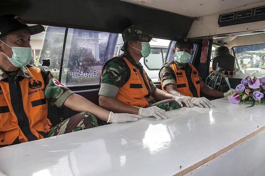 Indonesian officers sit next to a coffin contained a dead body of passenger of the AirAsia QZ8501 in Surabaya on Jan 3, 2015.&nbsp;-- PHOTO: AFP