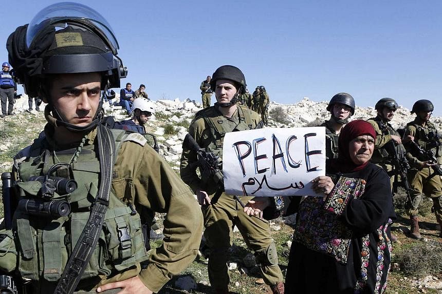 A protester holds a placard as she stands next to Israeli soldiers during a protest against Israeli settlements in Beit Fajjar town south of the West Bank city of Bethlehem on Dec 27, 2014.&nbsp;Israel will not permit its soldiers to be hauled in fro