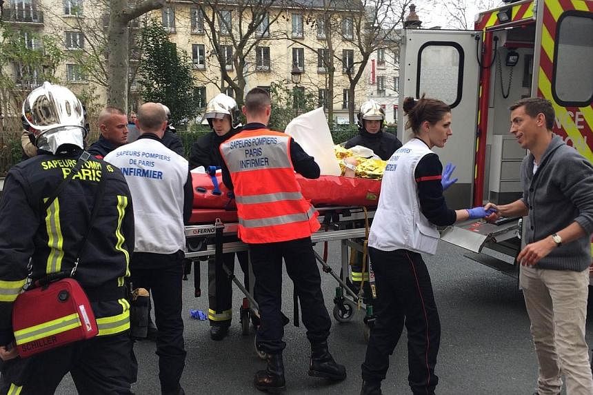 Firefighters carry an injured man on a stretcher in front of the offices of the French satirical newspaper Charlie Hebdo in Paris on Jan 7, 2015, after armed gunmen stormed the offices leaving at least 10 people dead.&nbsp;-- PHOTO: AFP