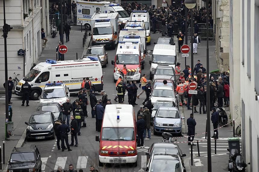 A general view shows firefighters, police officers and forensics gathered in front of the offices of the French satirical newspaper Charlie Hebdo in Paris on Jan 7, 2015, after armed gunmen stormed the offices leaving twelve dead. -- PHOTO: AFP