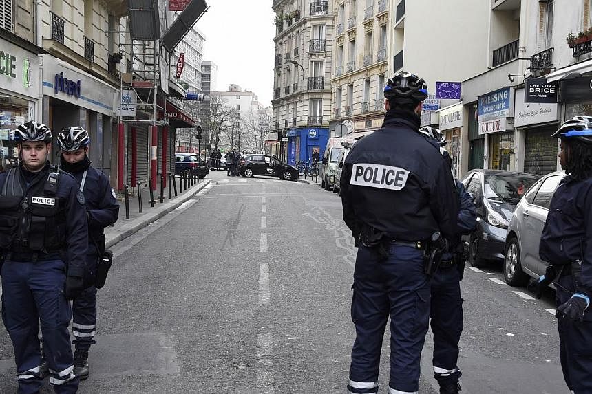 French police officers stand in a street as forensic experts examine the car (back, centre) used by armed gunmen who stormed the Paris offices of satirical newspaper Charlie Hebdo, killing 12 people, on Jan 7, 2015 in Paris. -- PHOTO: AFP