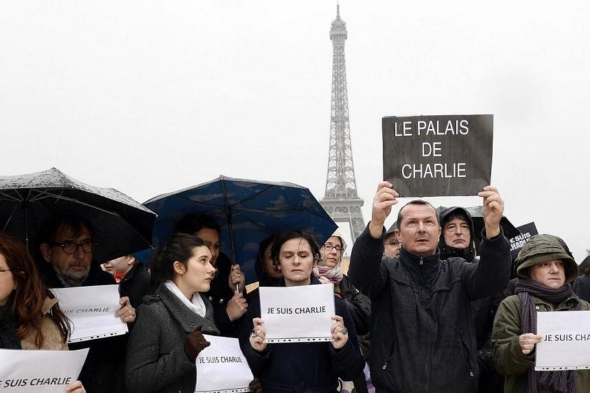 A man holds a sign reading "The palace of Charlie" as people observe a minute of silence in front of the Eiffel Tower in Paris on Jan 8, 2015, in honour of the 12 people killed by extremists at a magazine known for publishing cartoons deemed offensiv