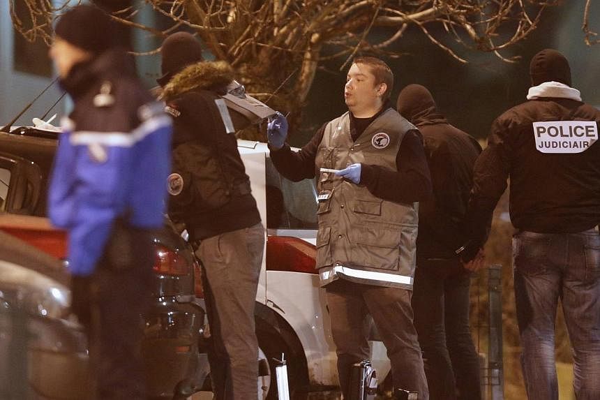 Police investigators search for evidence as an unidentified man is detained (2nd from right) during an operation in the eastern French city of Reims Jan 8, 2015, after the shooting against the Paris offices of Charlie Hebdo, a satirical newspaper.&nb