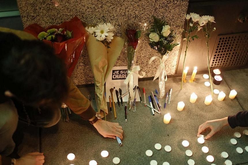 Two demonstrators place a candle and pen at a makeshift memorial outside the Consulate General of France during a vigil to pay tribute to the victims of an attack on satirical magazine Charlie Hebdo in Paris, in San Francisco, California on Jan 7, 20