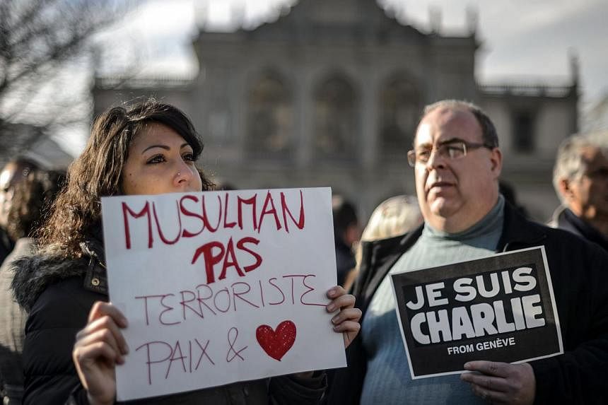 People hold placards reading in French "Muslim not terrorists, peace and love" and "I am Charlie from Geneva" (right) during a gathering in the centre of Geneva on Jan 8, 2015 to pay tribute to the 12 people killed the day before in an attack by arme