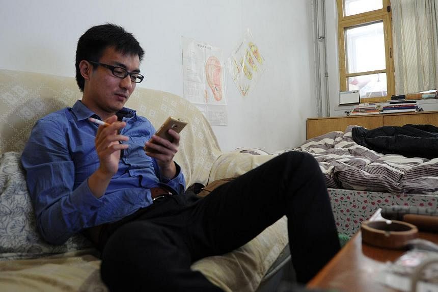 This picture taken on Dec 15, 2014, shows A Qi using his phone as he smokes in his rented home in Beijing. Mr Zhao Jun, 30, has no girlfriend, no savings and a dull job with bad pay, a typical "diaosi" as they are called, meaning the millions of "los