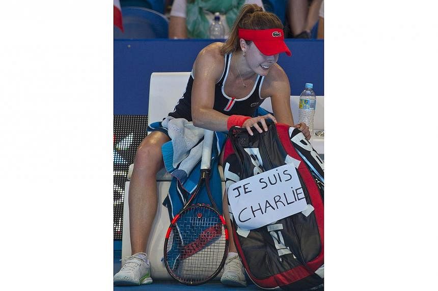 Alize Cornet of France displays a sign on her bag (right) of her support for Charlie Hebdo magazine during a break between games in her match against Agnieszka Radwanska of Poland during their women's singles match on day six of the Hopman Cup tennis