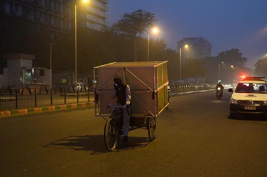 An Indian cycle rickshaw puller transports a rack of shelves as he speaks on his mobile phone at dusk in New Delhi on Jan 4, 2015. -- PHOTO: AFP