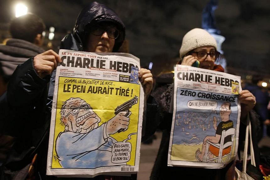 Women hold Charlie Hedbo's frontpages during a gathering on the Place de Republique (Republic square) in Paris, on Jan 8, 2015, as a tribute to the 12 people killed by two gunmen at the French weekly newspaper Charlie Hebdo's editorial office. -- PHO