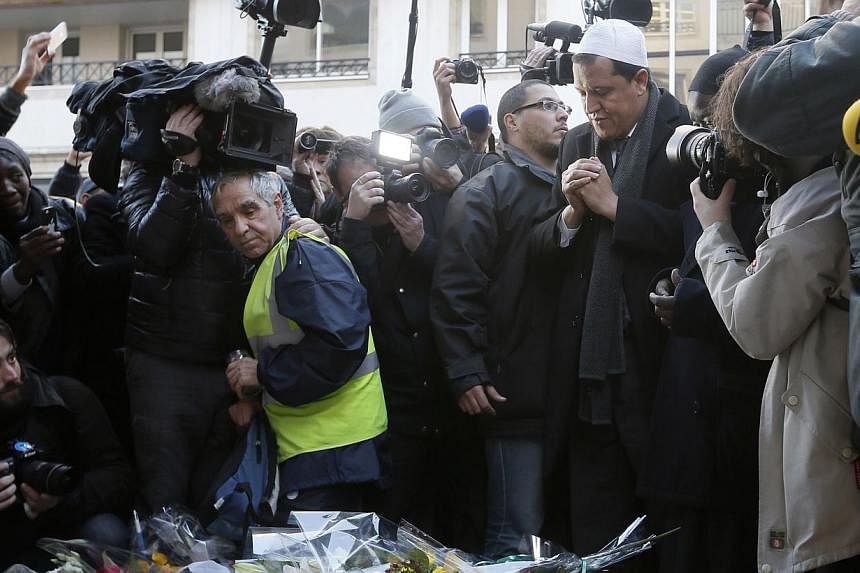 Hassen Chalghoumi (right), Imam of the municipal Drancy mosque in Seine-Saint-Denis, is surrounded by journalists as he pays his respects outside the offices of weekly satirical newspaper Charlie Hebdo in Paris Jan 8, 2015.&nbsp;French imams condemne