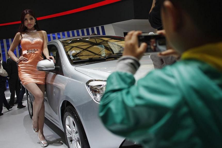 A child takes a picture of a model as she poses next to a car during the the 15th Shanghai International Automobile Industry Exhibition in Shanghai, on April 21, 2013. -- PHOTO: REUTERS