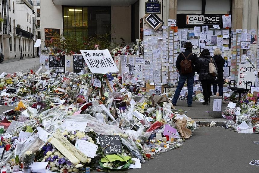People visit a makeshift memorial near the Paris headquarters of the French satirical weekly Charlie Hebdo on Jan 12, 2015, in tribute to the 17 victims of a three-day killing spree by homegrown Islamists.&nbsp;This week's edition will defiantly feat