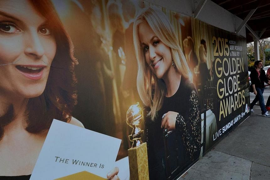 Commuters walk past a poster showing the Golden Globe Award hosts Tina Fey (left) and Amy Poehler (right) in Beverly Hills. The comic duo will present the Globes for a third and final year today in what organizers hope will continue its ratings winni