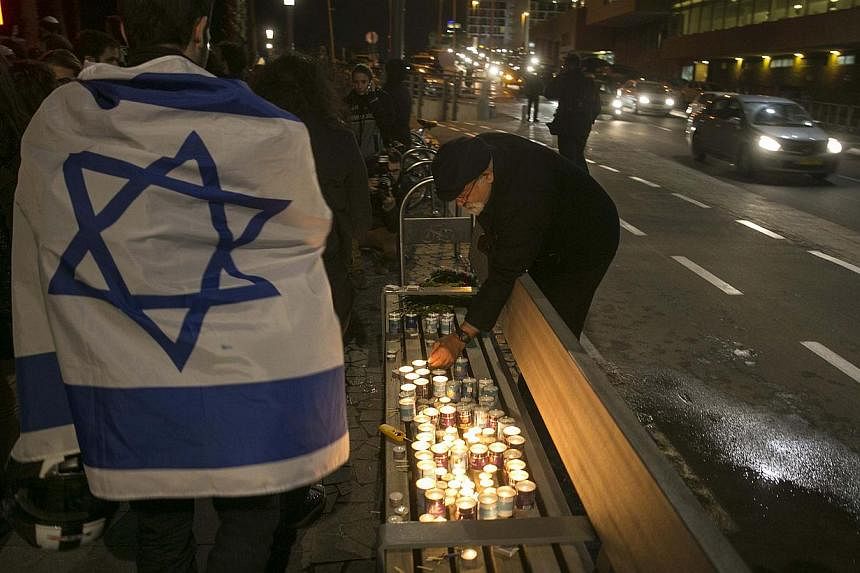 A man lights candles as another draped in an Israeli flag walks by during a tribute for the victims of the shootings at the satirical weekly newspaper Charlie Hebdo and a Jewish deli in Paris, -- PHOTO: REUTERS