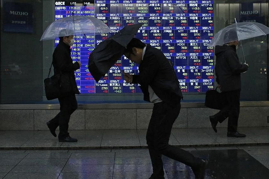 Pedestrians, holding umbrellas, walk past an electronic board showing stock prices outside a brokerage in Tokyo on Jan 15, 2015. -- PHOTO: REUTERS