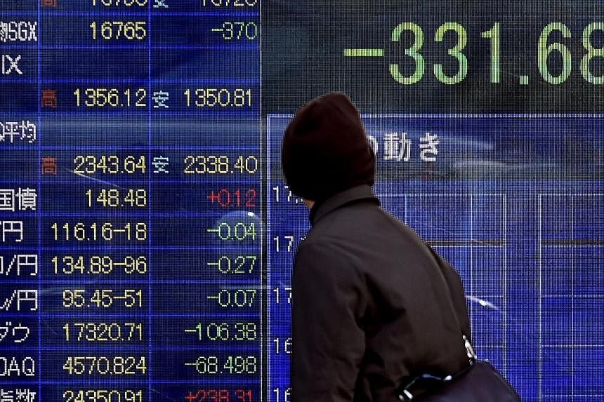 A pedestrian looking at a share prices board in Tokyo on Jan 16, 2015. Asian shares fell on Friday and major currencies mostly stuck to late US levels as investors react to Switzerland's unexpected move to abandon its currency cap. -- PHOTO: AFP