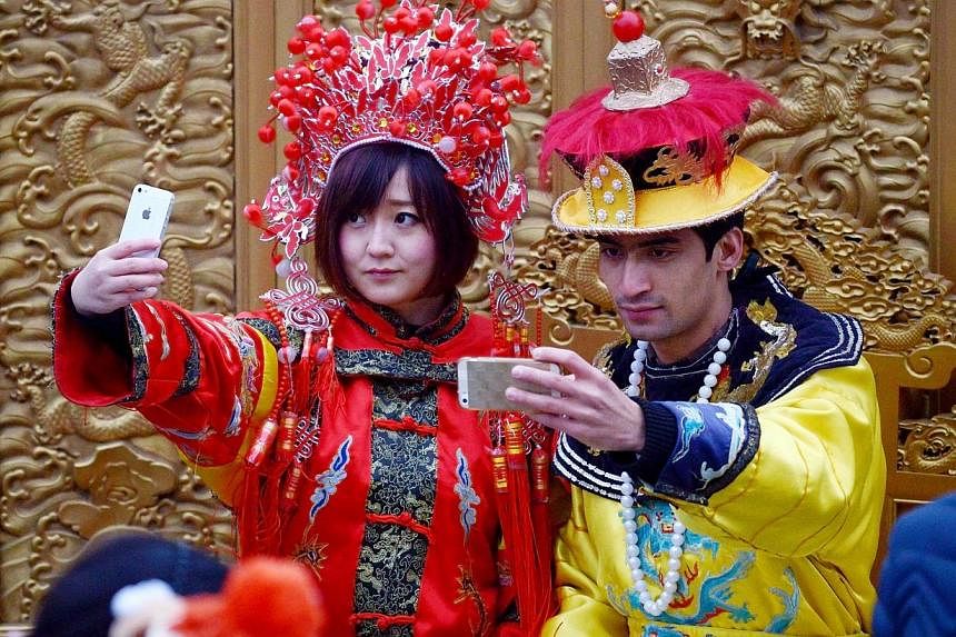 Two tourists dressed in Qing Dynasty clothing use their mobile phones to take a photo at a park in Beijing on Nov 27, 2014. -- PHOTO: AFP