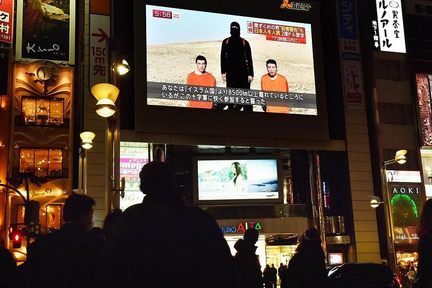 Passers-by&nbsp;on Jan 20, 2015,&nbsp;looking at a large TV screen in Tokyo broadcasting news reports about the two Japanese men (in orange) who have been kidnapped by ISIS. -- PHOTO: AFP