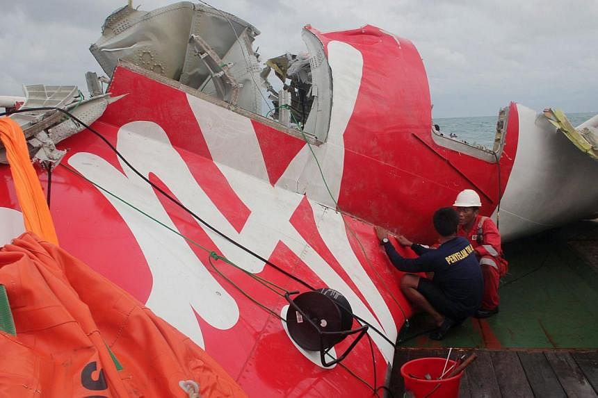 An Indonesian diver and an official examine the wreckage from AirAsia flight QZ8501 after it was lifted into the Crest Onyx ship at sea on Jan 10, 2015. -- PHOTO: AFP