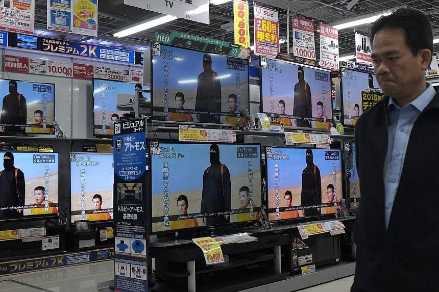 A man at an electronics store in Tokyo Jan 20, 2015,&nbsp;walking past television sets displaying a news programme about an ISIS video purporting to show two Japanese captives, Mr Kenji Goto and Mr Haruna Yukawa. -- PHOTO: REUTERS