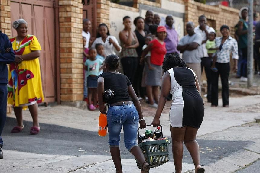 Locals look on as young women run with items from a shop believed to be owned by a foreigner, in Soweto on Jan 22, 2015.&nbsp;South African police said they had arrested 121 people on Friday after mobs went on a looting spree of grocery stores owned 